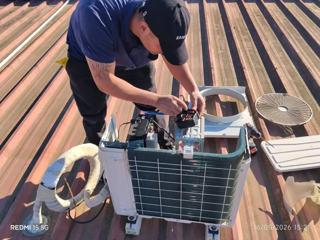 Técnico de reparación de aire acondicionado Samsung trabajando en la tarjeta electrónica de una unidad exterior en una azotea.